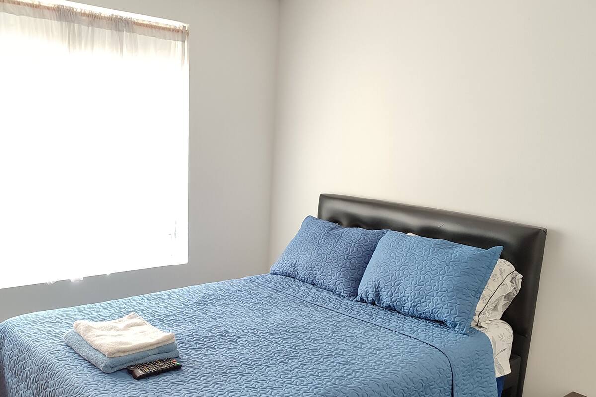 A neatly made bed with a blue quilt, a remote control, and folded towels on the bed.