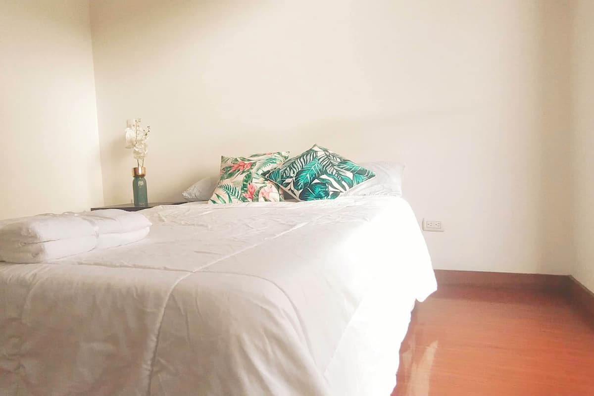 A neatly made bed with white linens, a decorative vase with flowers, and tropical patterned pillows.