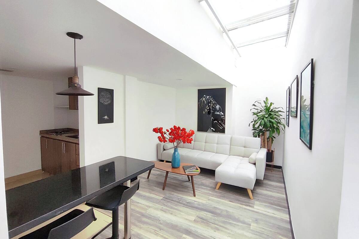 A modern kitchen with a dining area, a white sofa, and artwork on the walls.