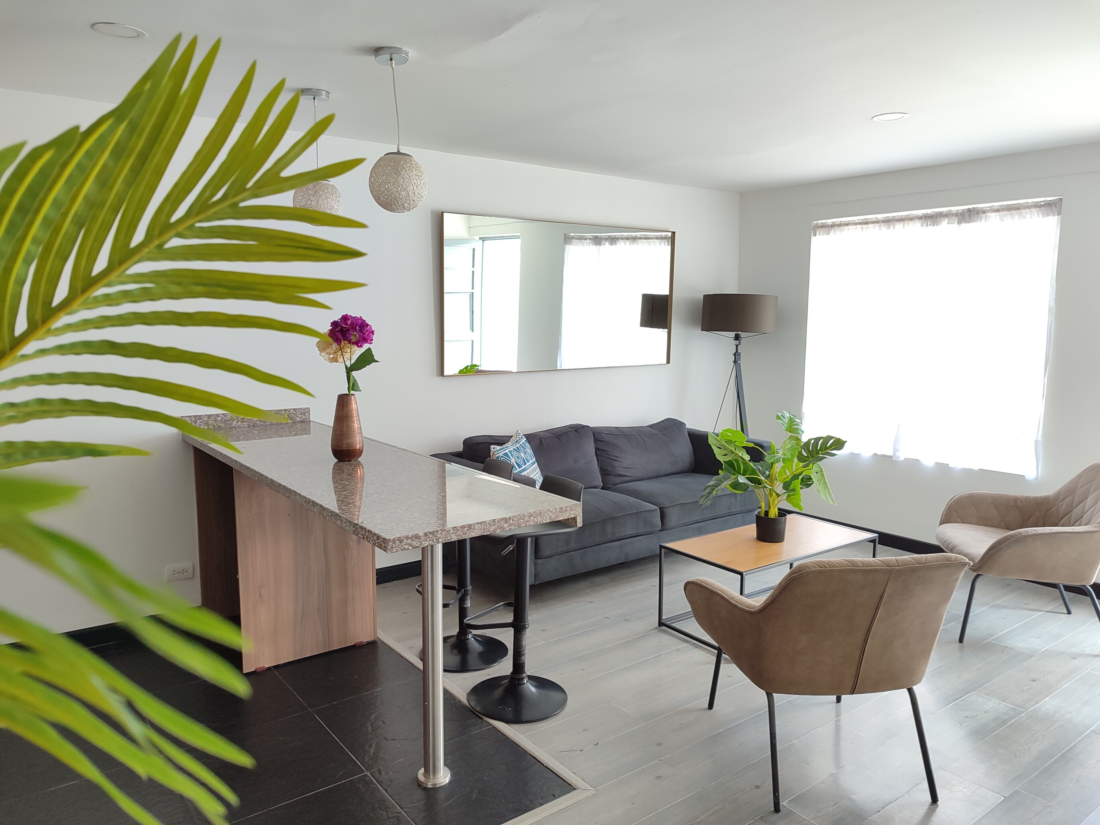 A modern living room with a sofa, coffee table, and chairs. There is a plant on the coffee table and a vase with flowers on the side table.