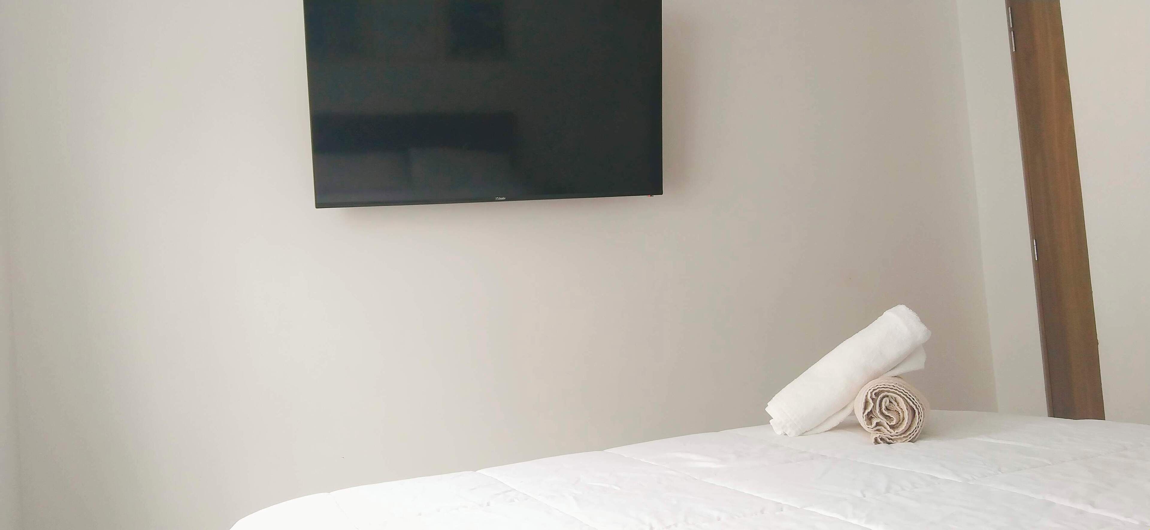 A neatly made bed with a rolled white towel, a plain wall, and a wooden door frame.