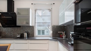 Una cocina moderna con armarios blancos, horno integrado y ventana con persianas.