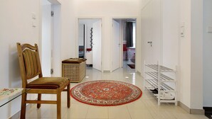 Un pasillo con una silla de madera, un tapete estampado, un zapatero y una puerta que da a otra habitación.