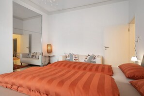 Un dormitorio con una cama grande, una mesita de noche con una lámpara, un espejo y un sofá al fondo.