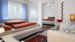 Habitación de hotel moderna con cama, sofá, espejo, candelabro y vistas a árboles a través del ventanal.