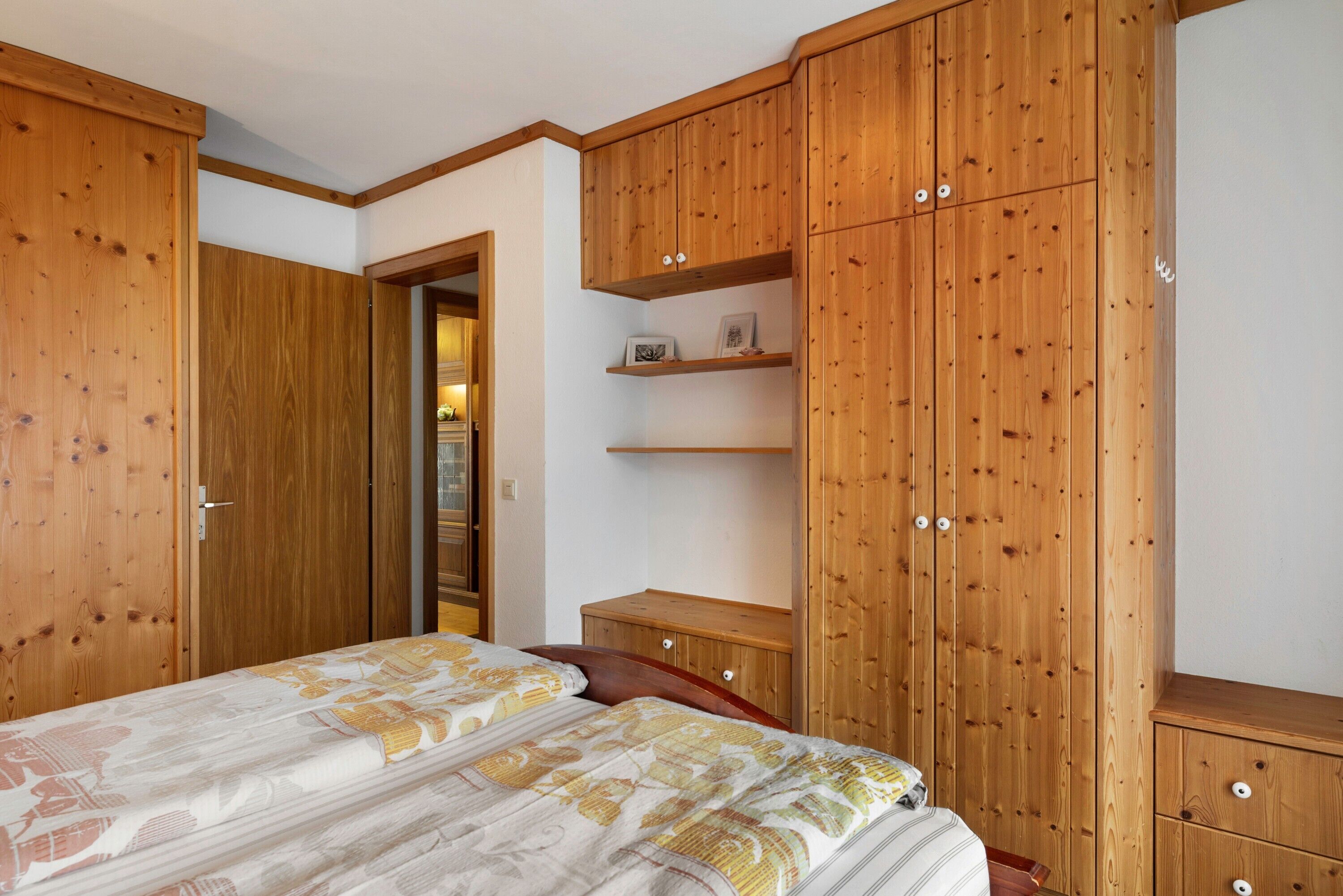 A bedroom with a bed, wooden wardrobe, and a small wooden nightstand.