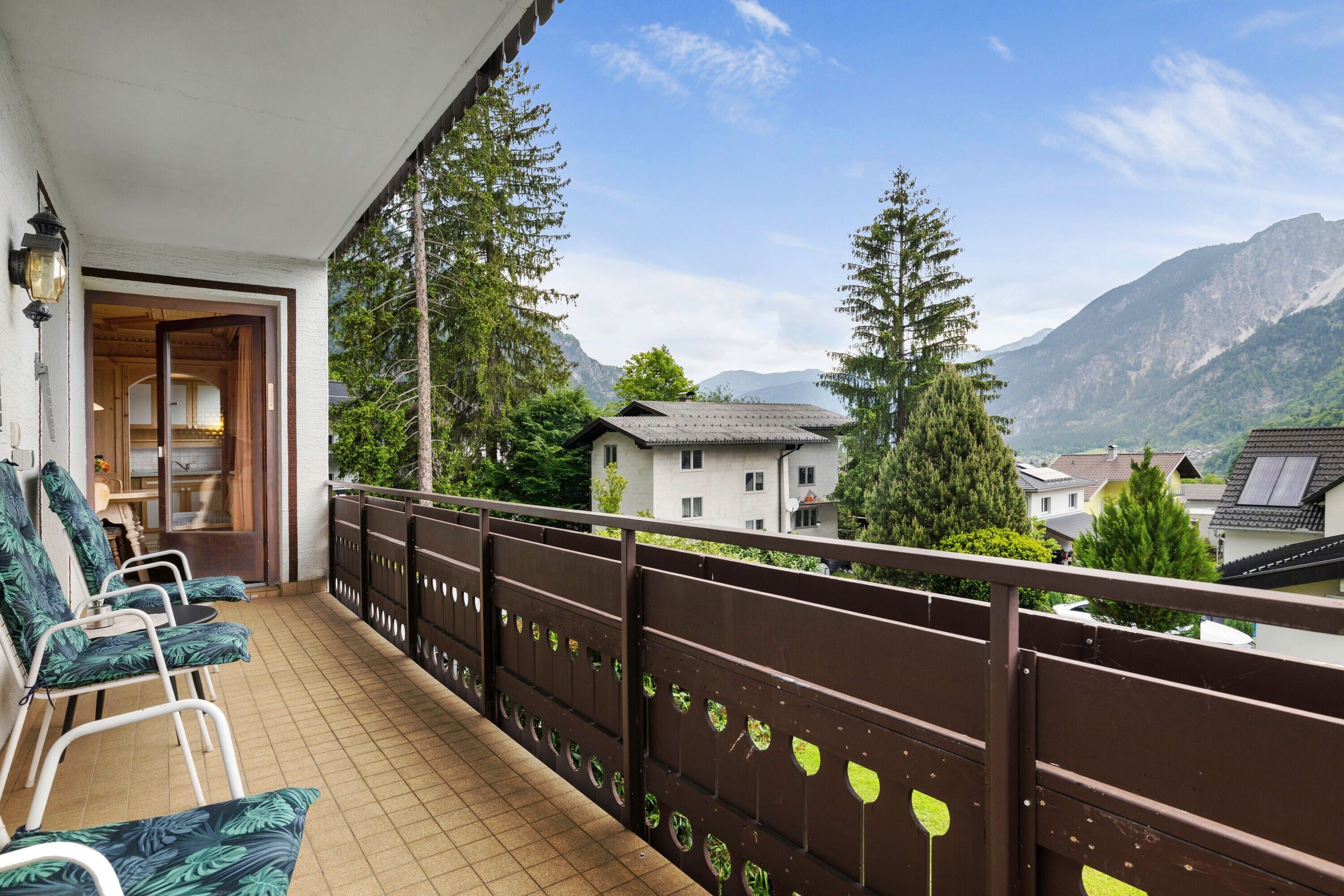 A balcony with chairs, a view of mountains, and a building in the background.