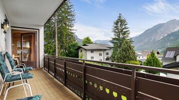 A balcony with chairs, a view of mountains, and a building in the background.