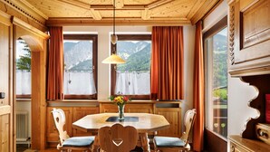 Ein Esszimmer mit Holzboden, einem Tisch und Stühlen, einer Vase mit Blumen und Blick auf Berge durch große Fenster.