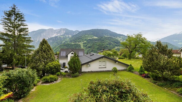 Ein Haus mit Schrägdach, umgeben von einem gepflegten Rasen und verschiedenen Bäumen.