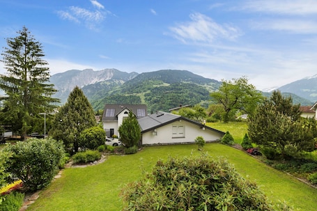 A house with a sloped roof, surrounded by a well-maintained lawn and various trees.. Apartment 'Jordis' with Mountain View, Private Terrace, garden and Wi-Fi