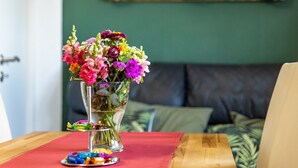 A dining table with a vase of colorful flowers, a plate with candies, and a green wall with a framed picture. - Apartment 'Baumelt' with Private Terrace, Shared Garden and Wi-Fi (Hechingen)