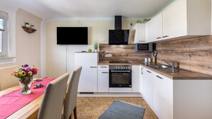 A modern kitchen with white cabinets, a wooden countertop, a built-in oven, and a flat-screen TV mounted on the wall. - Apartment 'Baumelt' with Private Terrace, Shared Garden and Wi-Fi (Hechingen)