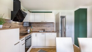 A modern kitchen with white cabinets, a herringbone wood floor, a built-in microwave, and a black range hood. - Apartment 'Baumelt' with Private Terrace, Shared Garden and Wi-Fi (Hechingen)