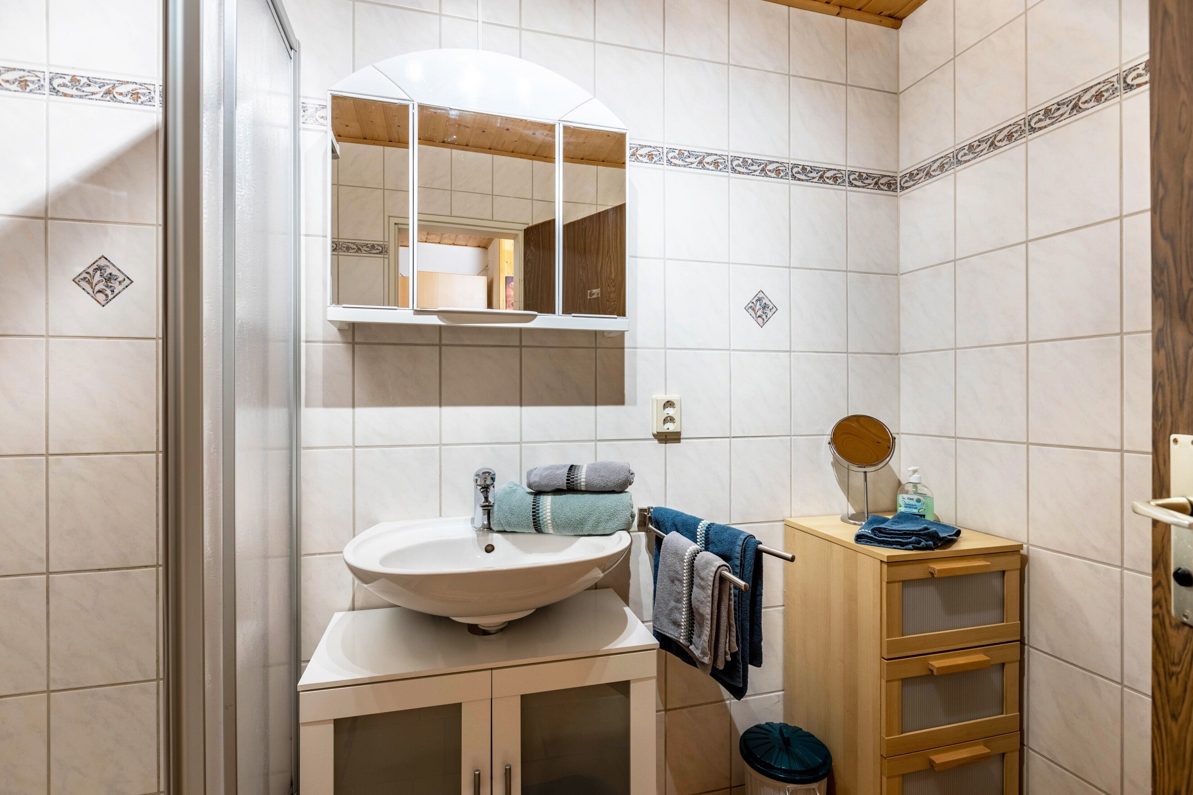 Een badkamer met een wastafel, spiegel, handdoekhouder en een houten kastje.