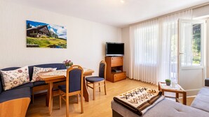 Una habitación amoblada con sofá, mesa de comedor, sillas, televisor y ventana con cortinas.