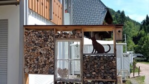 Una casa con cerca de madera, la silueta de un perro y una pila de leña.