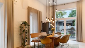 Un espace repas comprenant une table en bois, des chaises jaunes, un banc et des luminaires suspendus.