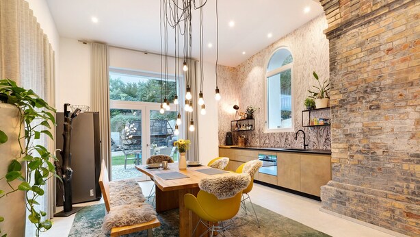 Une cuisine moderne avec un mur en briques, un coin repas avec des chaises jaunes et une grande fenêtre.