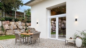 Une terrasse avec une table et des chaises, un pot de fleurs et un mur en pierre.