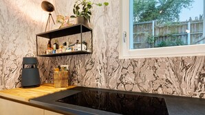 Une cuisine dotée d’un plan de travail noir, d’une cuisinière encastrée, d’une étagère contenant des ustensiles de cuisine et d’une fenêtre donnant sur un paysage verdoyant.