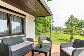 Une terrasse extérieure aménagée avec des meubles en osier, une plante en pot et une vue sur un paysage verdoyant.