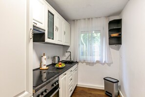 Une cuisine compacte avec des meubles blancs, un plan de travail noir, un évier en acier inoxydable et une fenêtre ornée de rideaux légers.