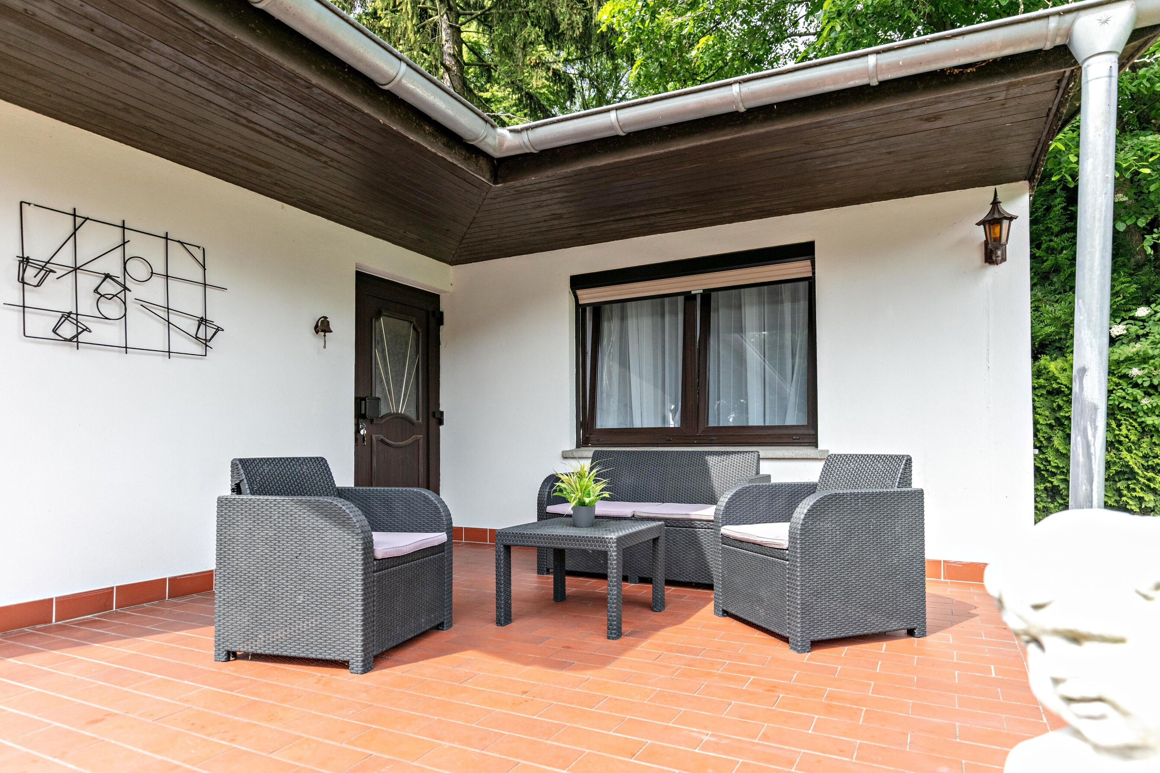 Eine überdachte Terrasse mit Korbmöbeln, einem kleinen Tisch und einem Blumentopf.