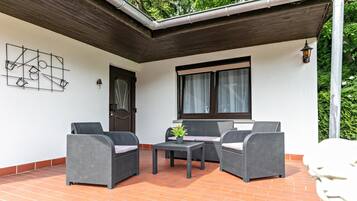 Eine überdachte Terrasse mit Korbmöbeln, einem kleinen Tisch und einem Blumentopf.
