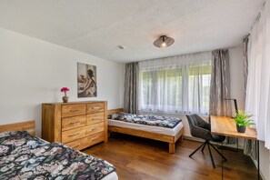 Une chambre avec deux lits, une commode en bois, un bureau avec une chaise et une fenêtre avec des rideaux.