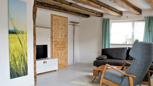 Ein Wohnzimmer mit Holzboden, einer Couch, einem Sessel, einer TV-Konsole und einem Gemälde.