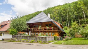 A wooden chalet with a sloped roof, a balcony with hanging flower baskets, and a stone wall in the foreground. - Apartment 'Haus Miriam' with Mountain View, Shared Garden and Wi-Fi (Münstertal)
