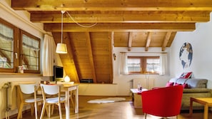 A cozy room with a wooden ceiling, a dining table with chairs, a red chair, a sofa, and a globe wall decoration.