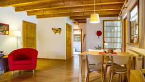 Habitació amb sostre de fusta, taula de dinar amb cadires, butaca vermella i finestra amb cortines.