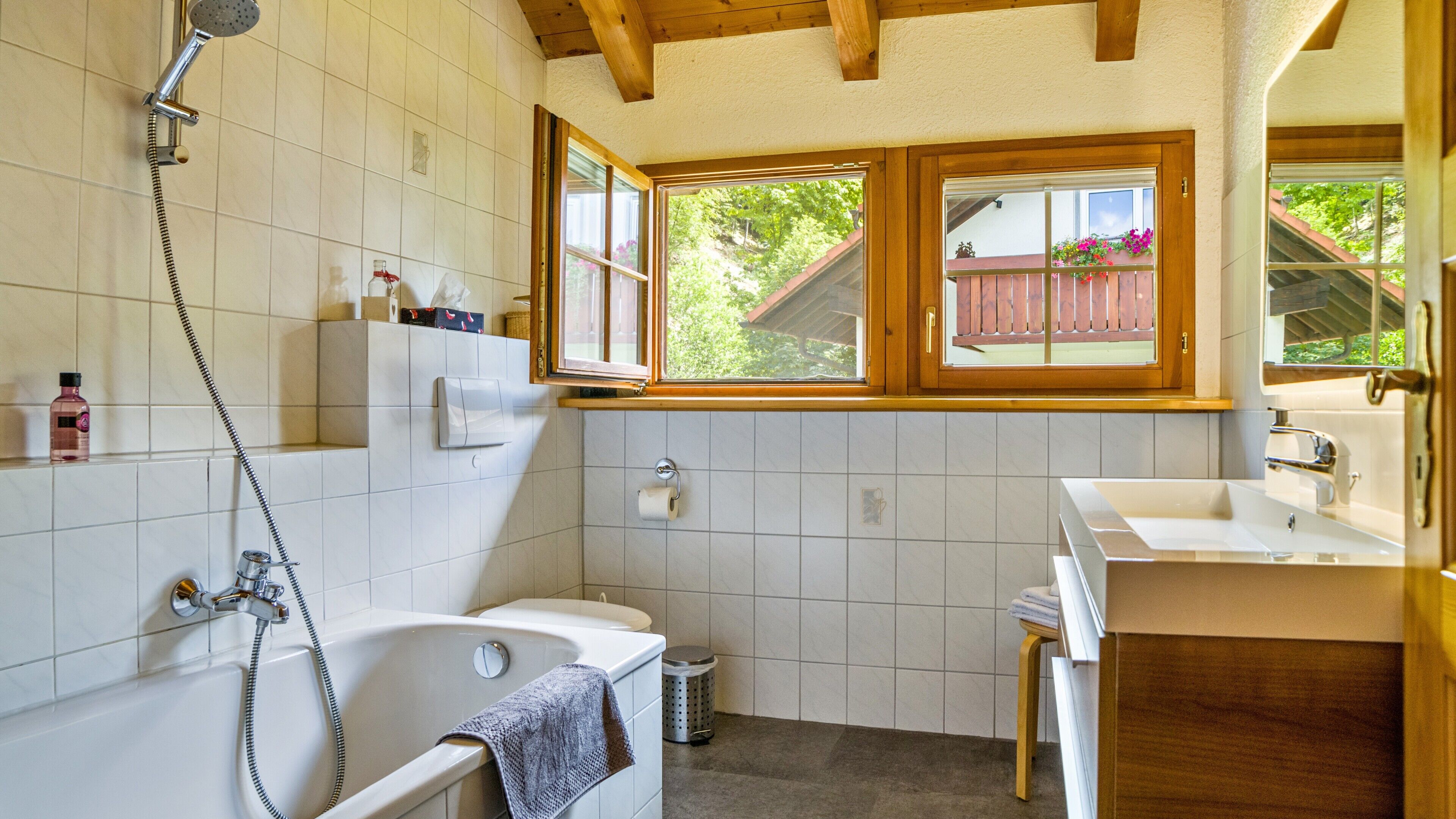 A bathroom with a bathtub, a shower, a toilet, and a sink. There are windows with a view of greenery outside.