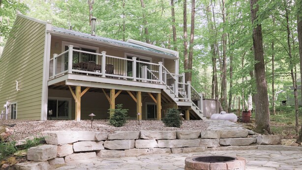 A two-story cabin with a balcony, stone steps, and a fire pit. - The best patio and firepit at The Cat's Lair in the woods!  Level 2 EV charger! (Egg Harbor)