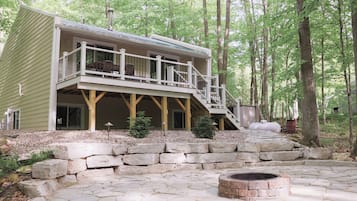 A two-story cabin with a balcony, stone steps, and a fire pit.