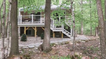 A cabin with a deck and stairs, surrounded by trees and a stone pathway.
