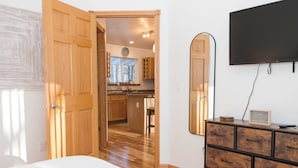 A bedroom with a wooden door, a dresser, and a TV mounted on the wall. - The best patio and firepit at The Cat's Lair in the woods!  Level 2 EV charger! (Egg Harbor)