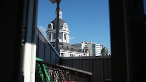 Vista d'un edifici amb cúpula i torre del rellotge, visible a través d'una finestra amb barana metàl·lica.