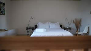 Un dormitori amb un llit gran, dues taules de nit amb làmpades, una cadira i un quadre a la paret.