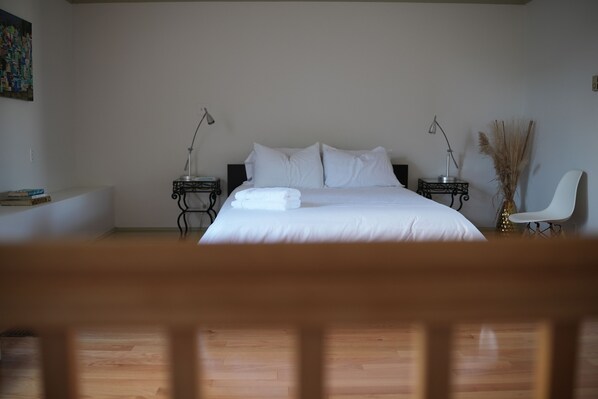 A bedroom with a large bed, two bedside tables with lamps, a chair, and a painting on the wall. - Unique, heritage building in the heart of Kingston! Right on Market Square!
(Kingston)