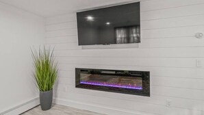 A modern room with a flat-screen TV mounted above a rectangular fireplace with a visible fire.
