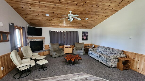 A cozy living room with a wooden ceiling, a fireplace, a TV, and comfortable seating. - Lazy Fox Lodge, Lake of the Woods
 (Baudette)