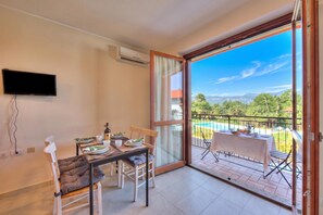 Ein Essbereich mit Tisch und Stühlen, einem an der Wand montierten Fernseher und einem Balkon mit Blick auf einen Pool.