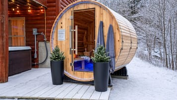 A wooden sauna with a curved roof, a bench inside, and two potted plants outside.