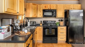 A kitchen with wooden cabinets, a black microwave, a black refrigerator, a stove, and a coffee bar. - Hot Tub, Sauna, Game Room, Fire Pit, BBQ, Karaoke, Dogs OK (Bethel)