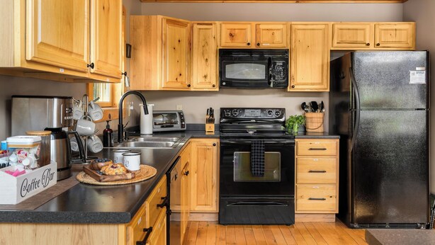 A kitchen with wooden cabinets, a black microwave, a black refrigerator, a stove, and a coffee bar. - Hot Tub, Sauna, Game Room, Fire Pit, BBQ, Karaoke, Dogs OK (Bethel)