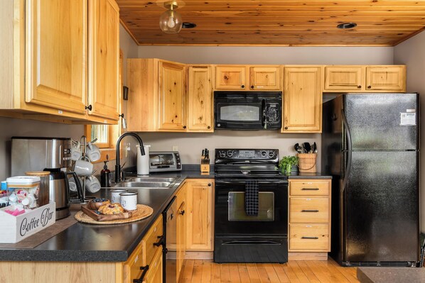 A kitchen with wooden cabinets, a black microwave, a black refrigerator, a stove, and a coffee bar.