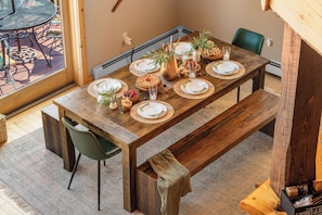 A wooden dining table set with plates, glasses, and a vase with greenery.